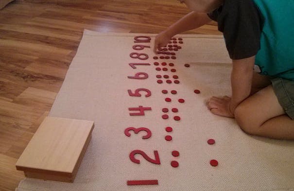 Child counting with number tiles and red dots on a mat