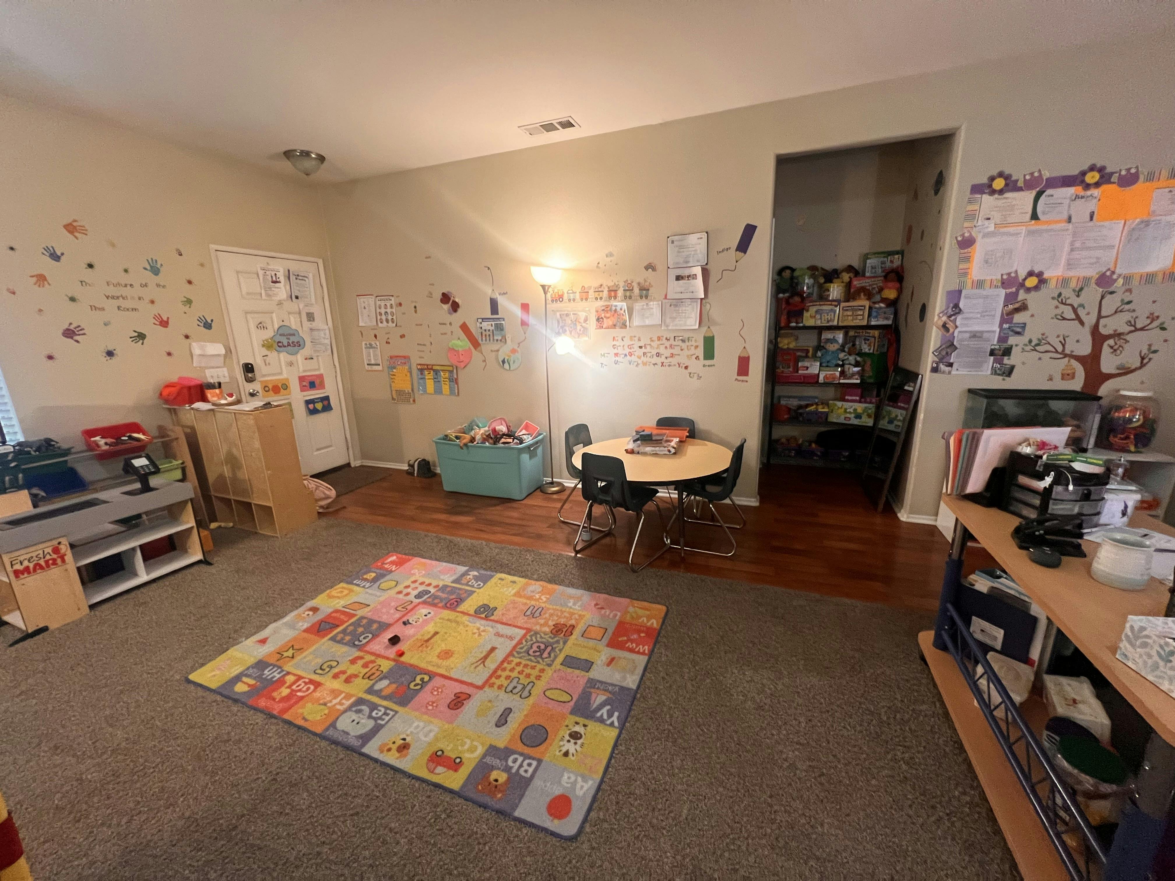 A classroom with a play kitchen, activity rug, and small table and chairs