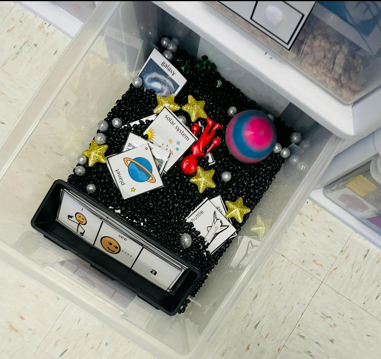 Sensory bin with black beads, star shapes, and planet cards