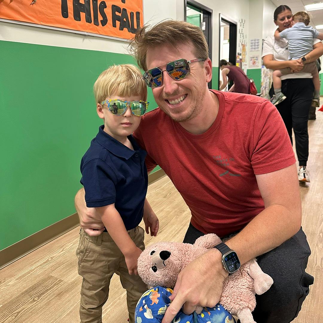 Adult and child wearing sunglasses, adult pointing at a stuffed animal