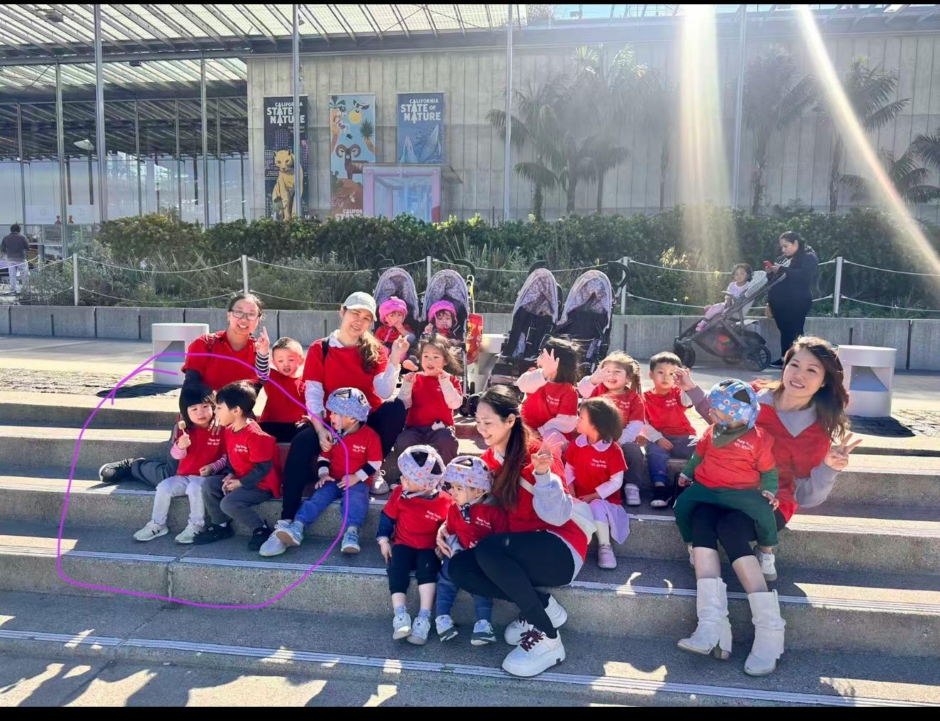 Group of adults and children in red shirts sitting on stairs outdoors