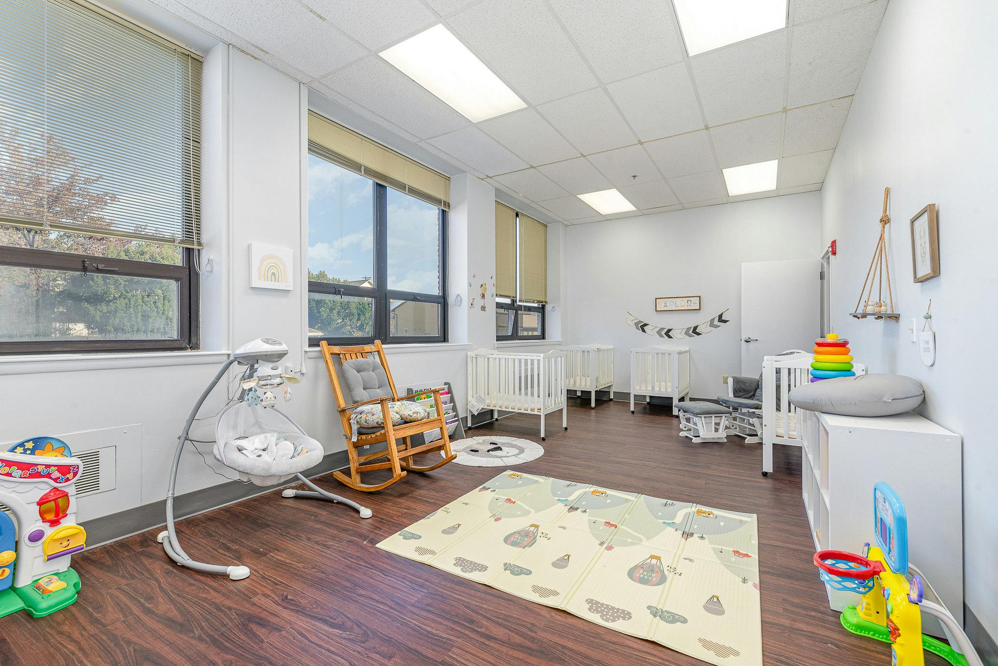 Nursery room with cribs, rocking chair, infant swing, and toys