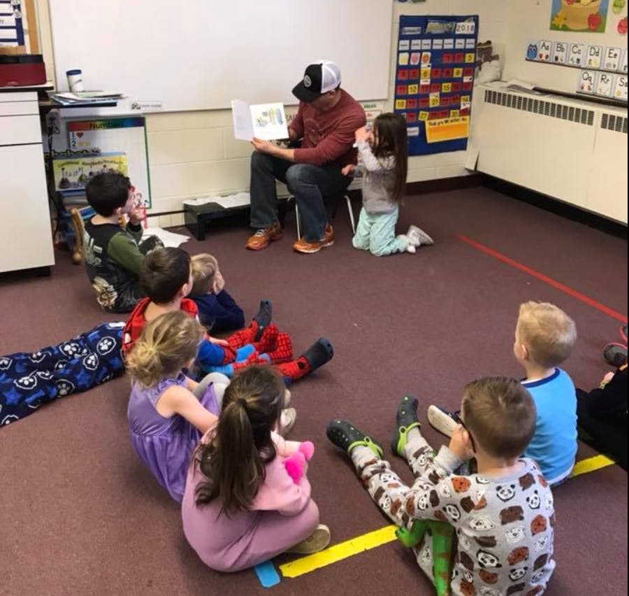 Person reading a book to a group of children in a classroom