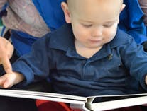 Child looking at a book with an adult's finger pointing