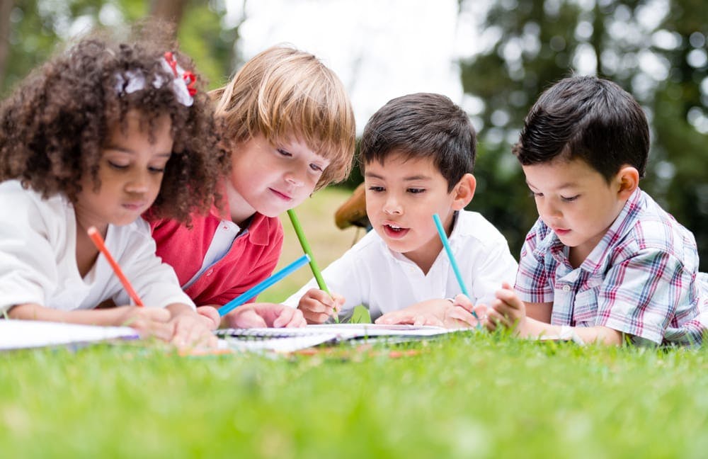 Four children drawing on paper with colored pencils outdoors