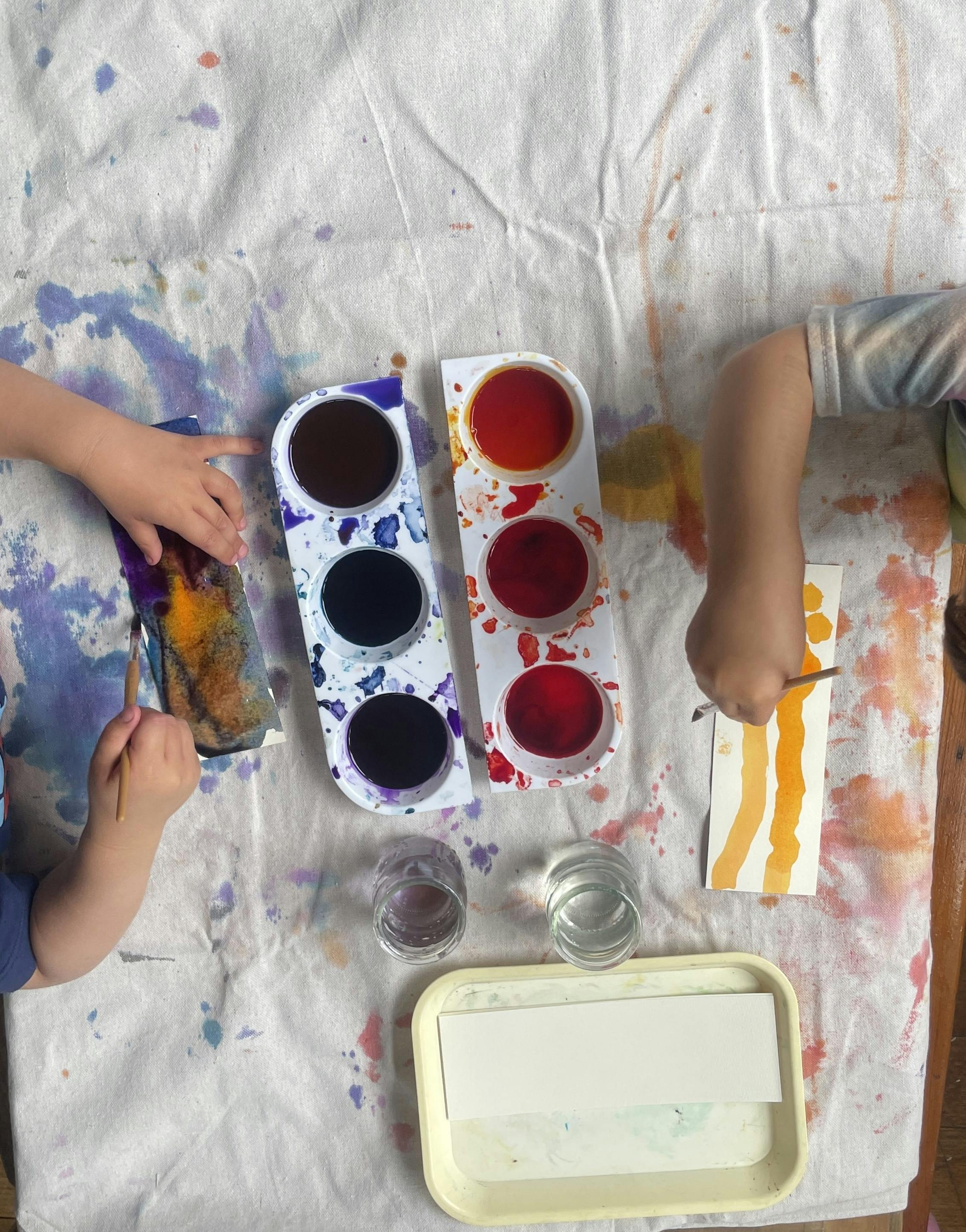 People painting on paper at a table with paint palettes and water