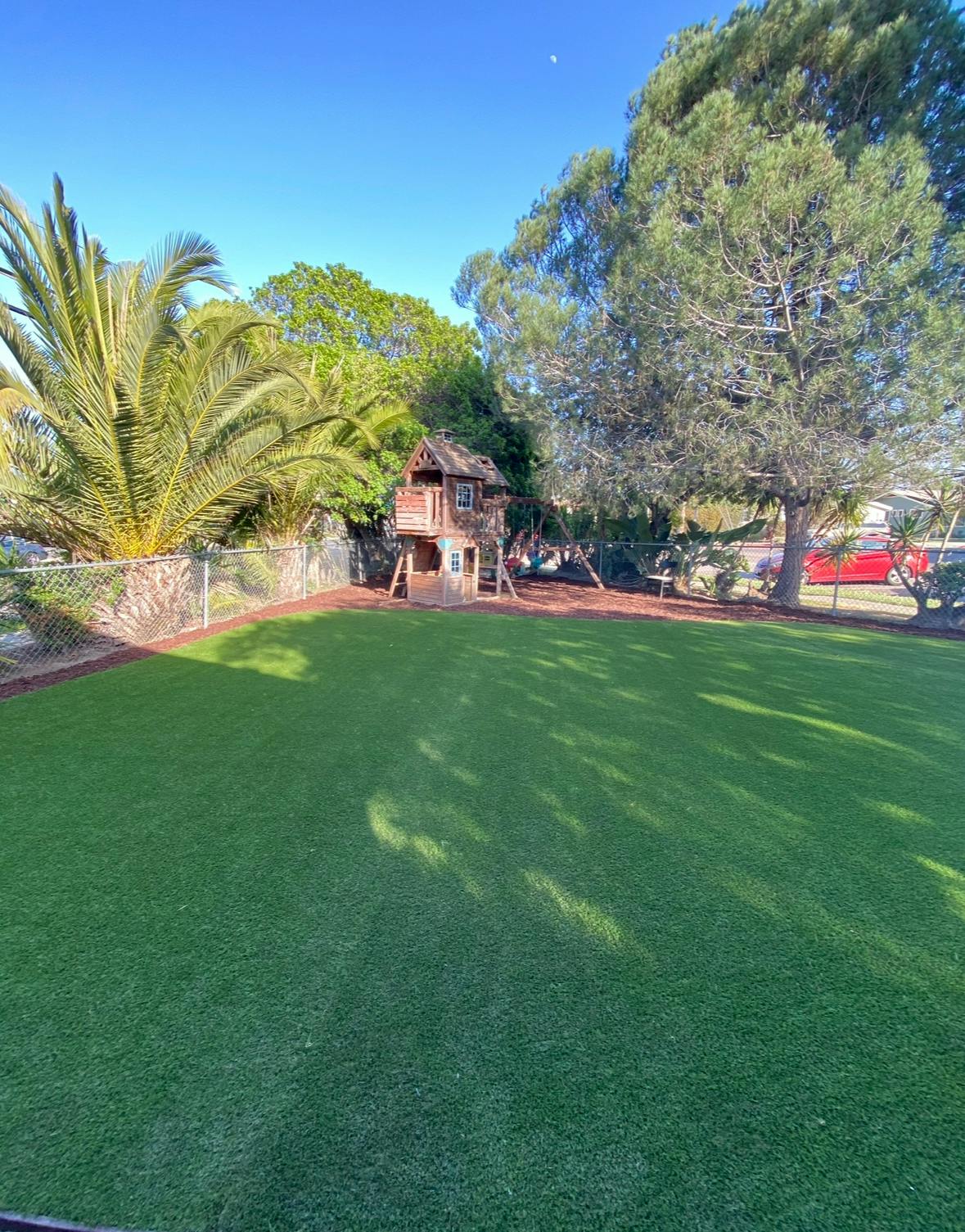 Grassy yard with a wooden playhouse and swing set under trees