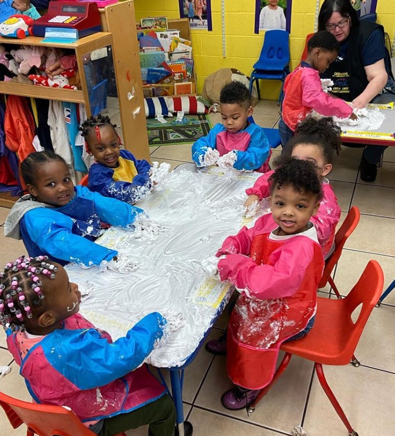 Children in smocks playing with white foam at a table