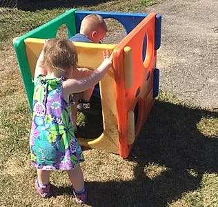 Two children playing in a colorful plastic play cube outdoors