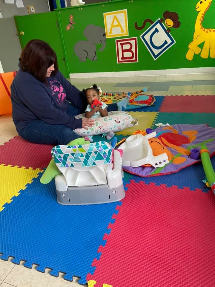 Person sitting on floor with a child holding a toy