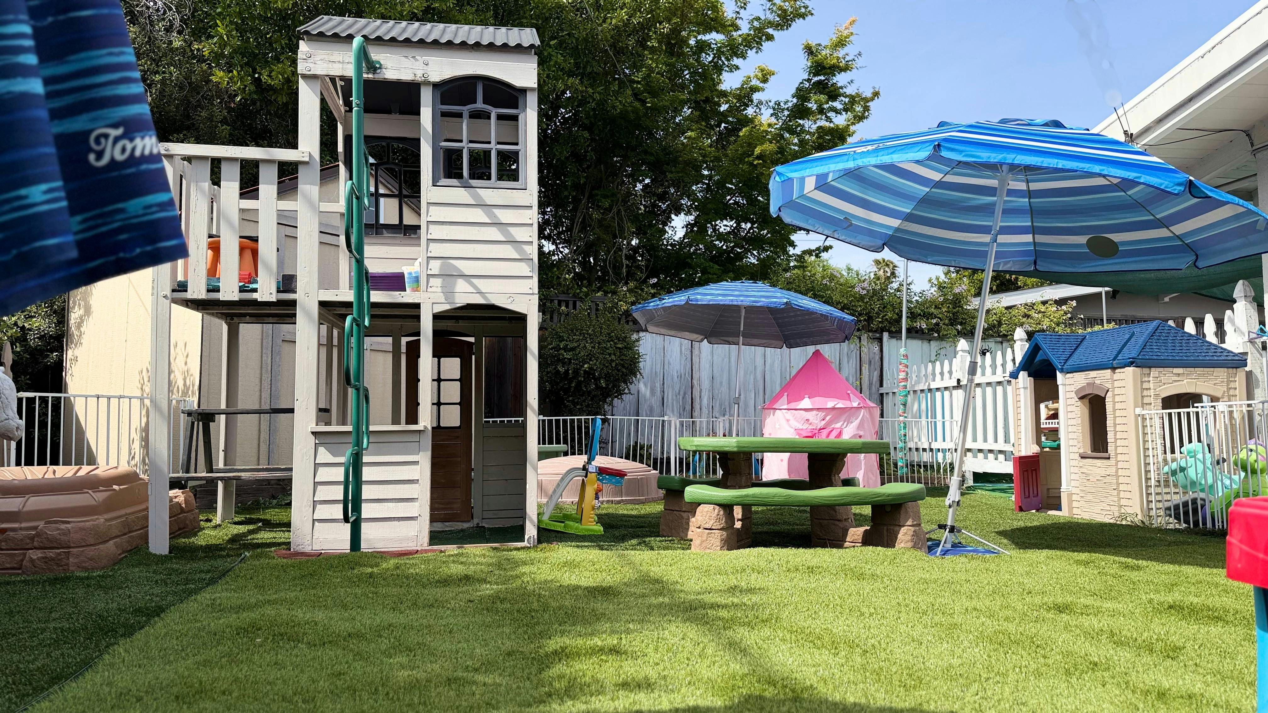 Playground with playhouse, picnic table, and blue umbrellas