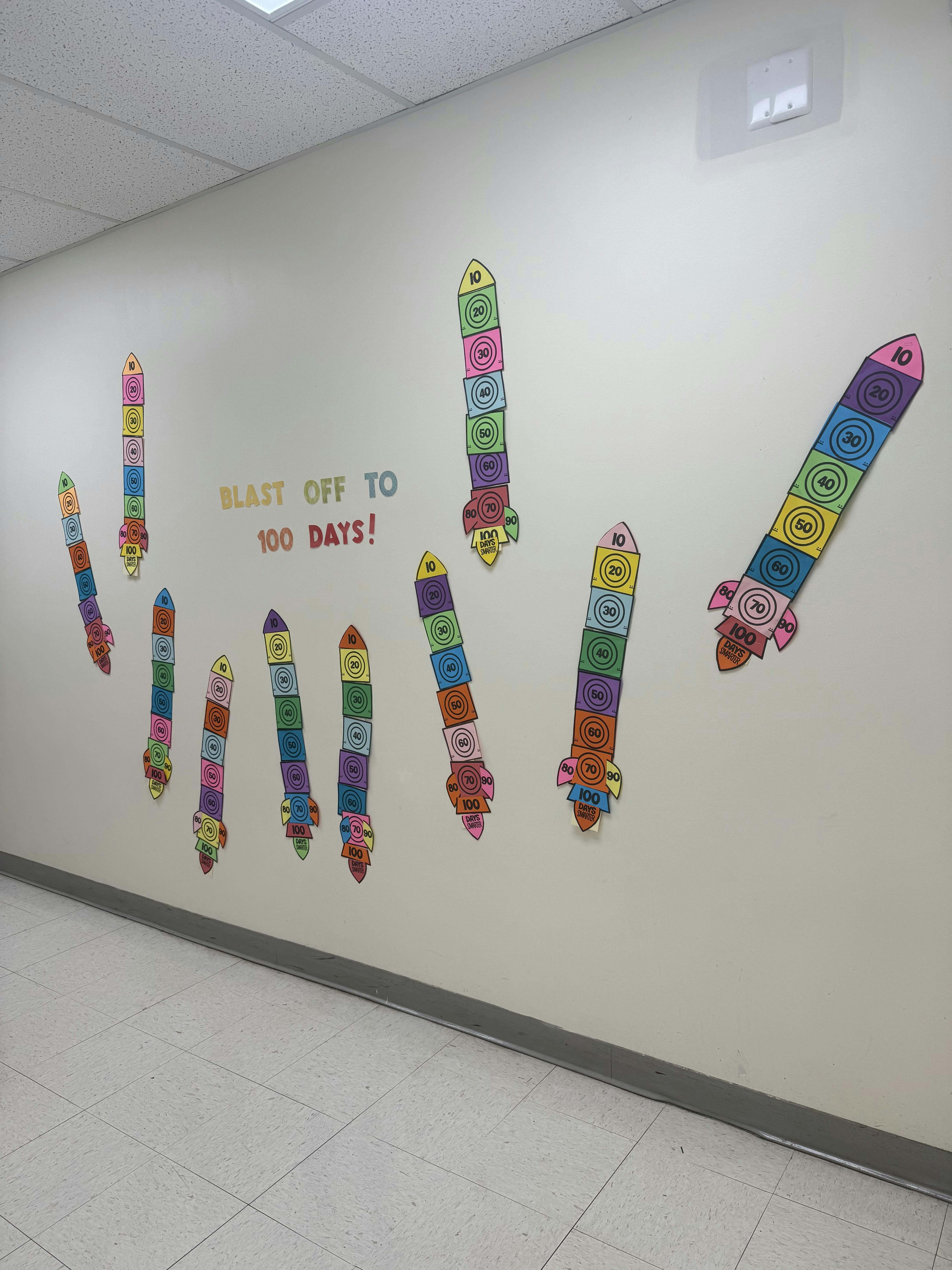 Classroom wall decorated with rocket cutouts showing numbers 10-100 and "Blast Off to 100 Days!" text