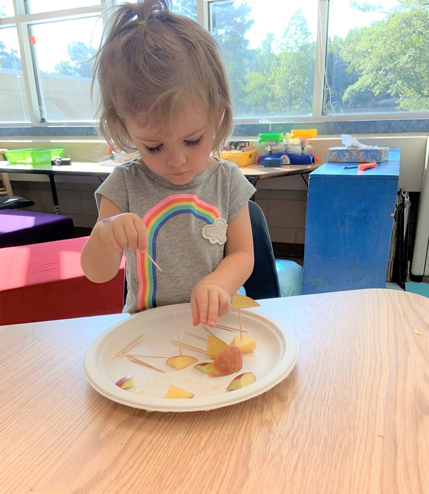 Child playing with food on a plate with toothpicks