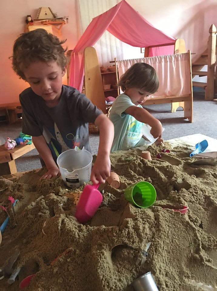 Two children playing in a sandpit with toys