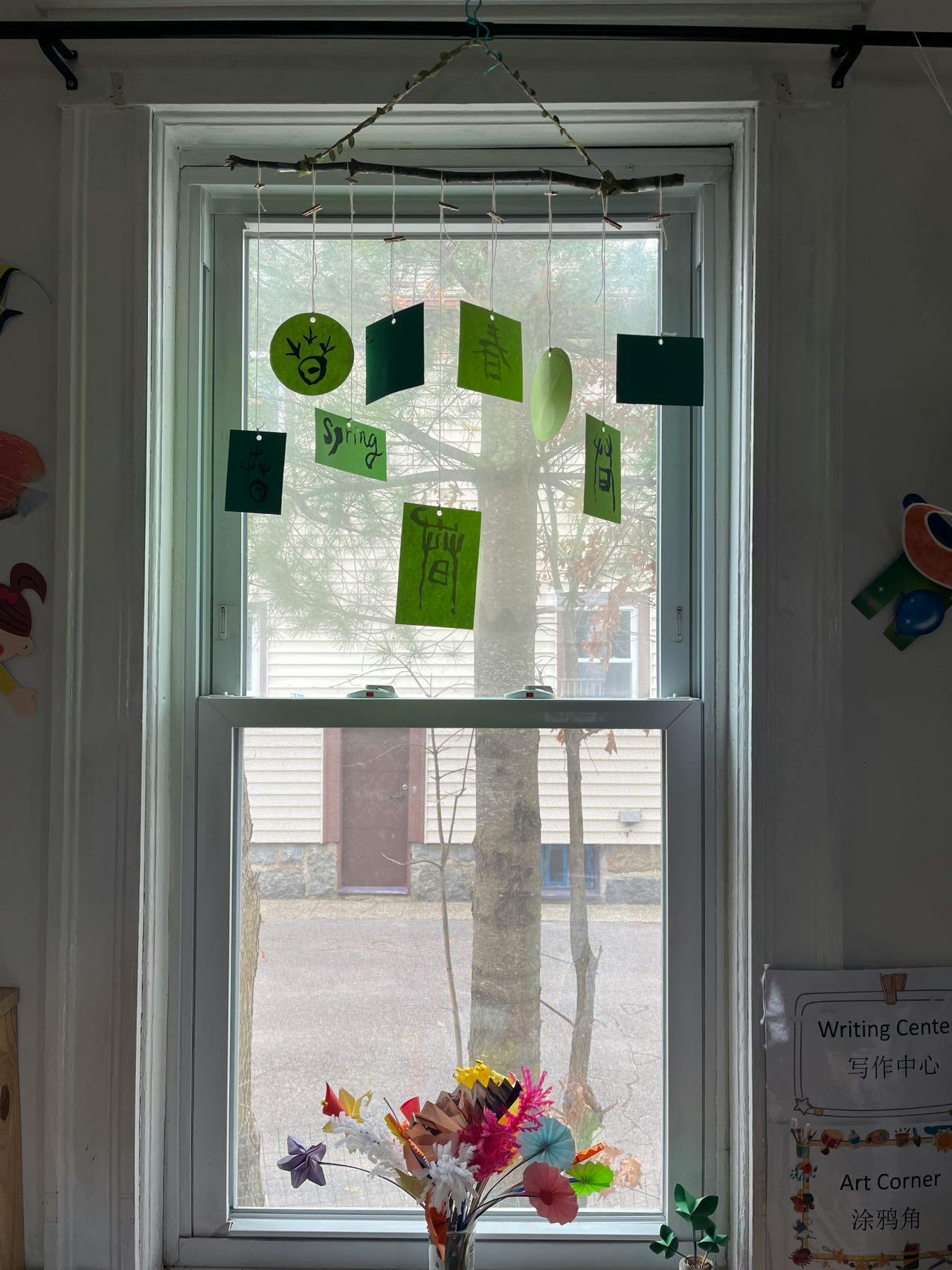 Window with green paper cutouts hanging from a branch