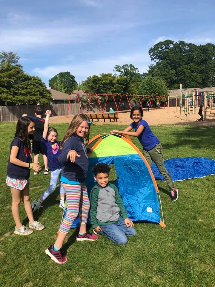 Children setting up a small tent on a grassy field