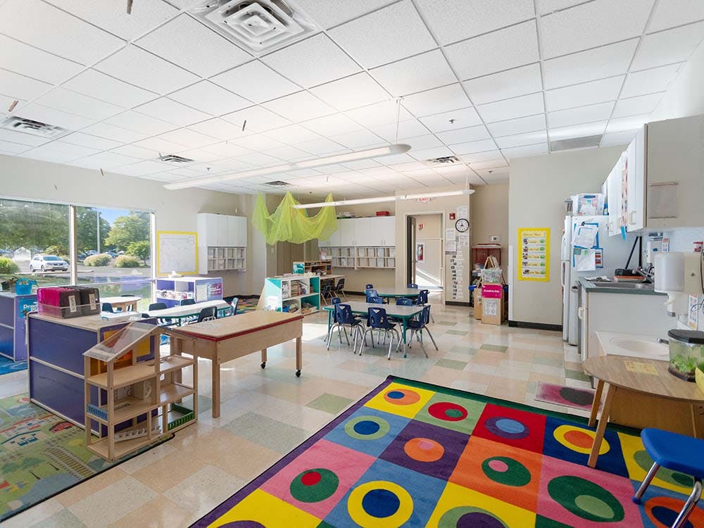 Colorful classroom with several tables and chairs, shelves, and a patterned rug