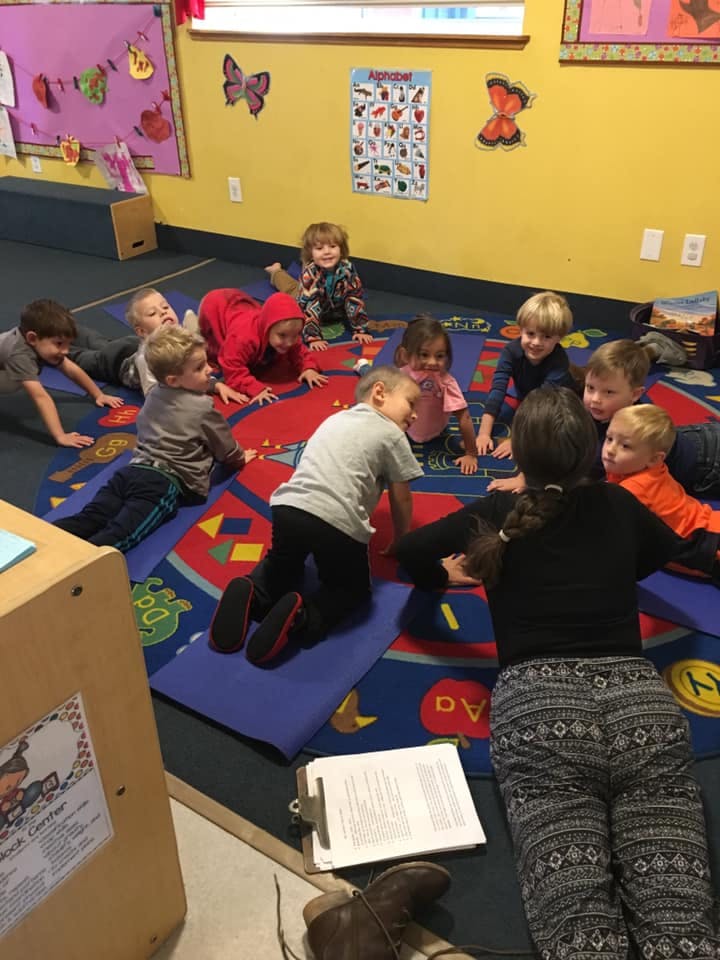 Children and an adult sitting on a colorful rug in a classroom