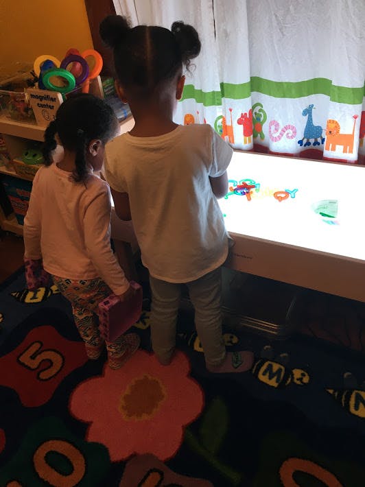 Two children playing with colorful objects on a light table