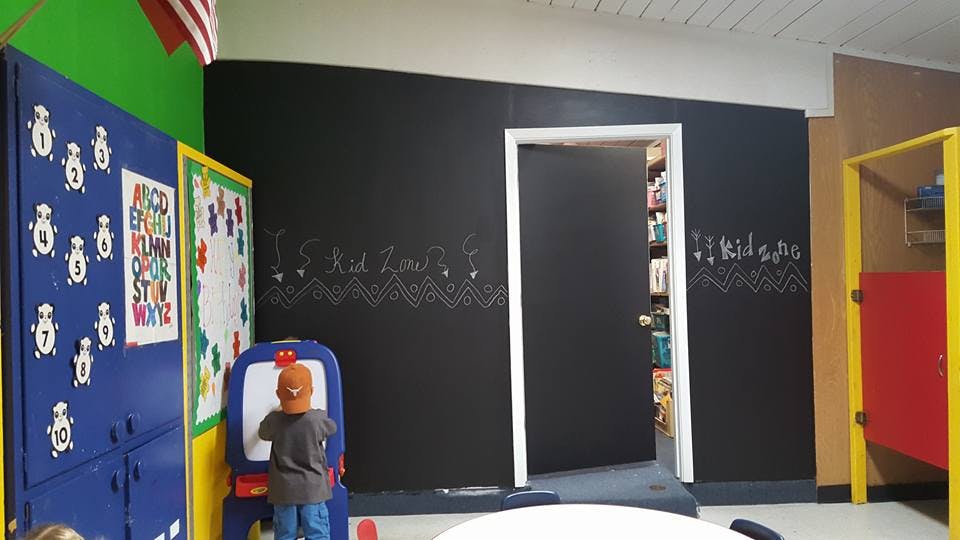 Child drawing on an easel in a room with a chalkboard wall