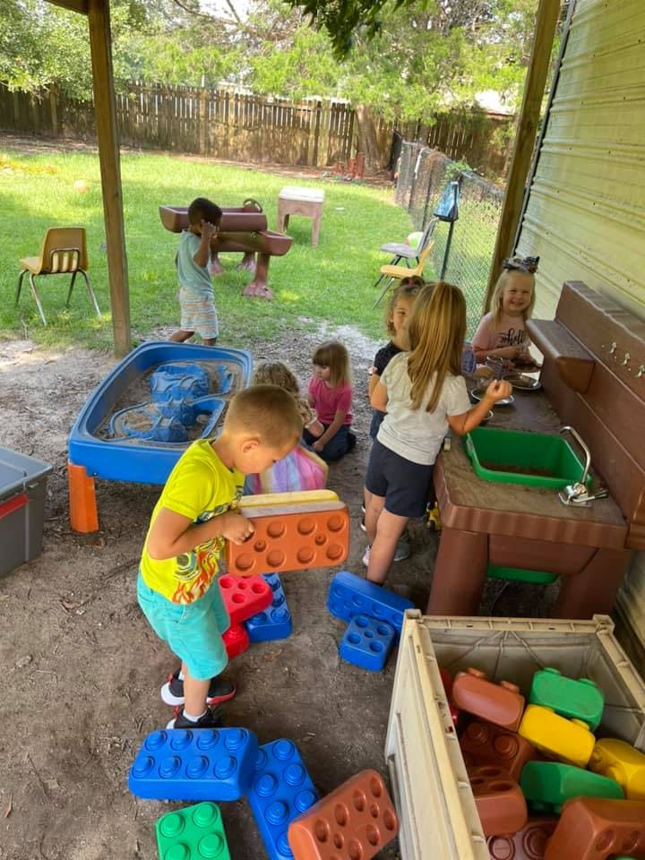 Children playing with large building blocks and a sand and water table outdoors