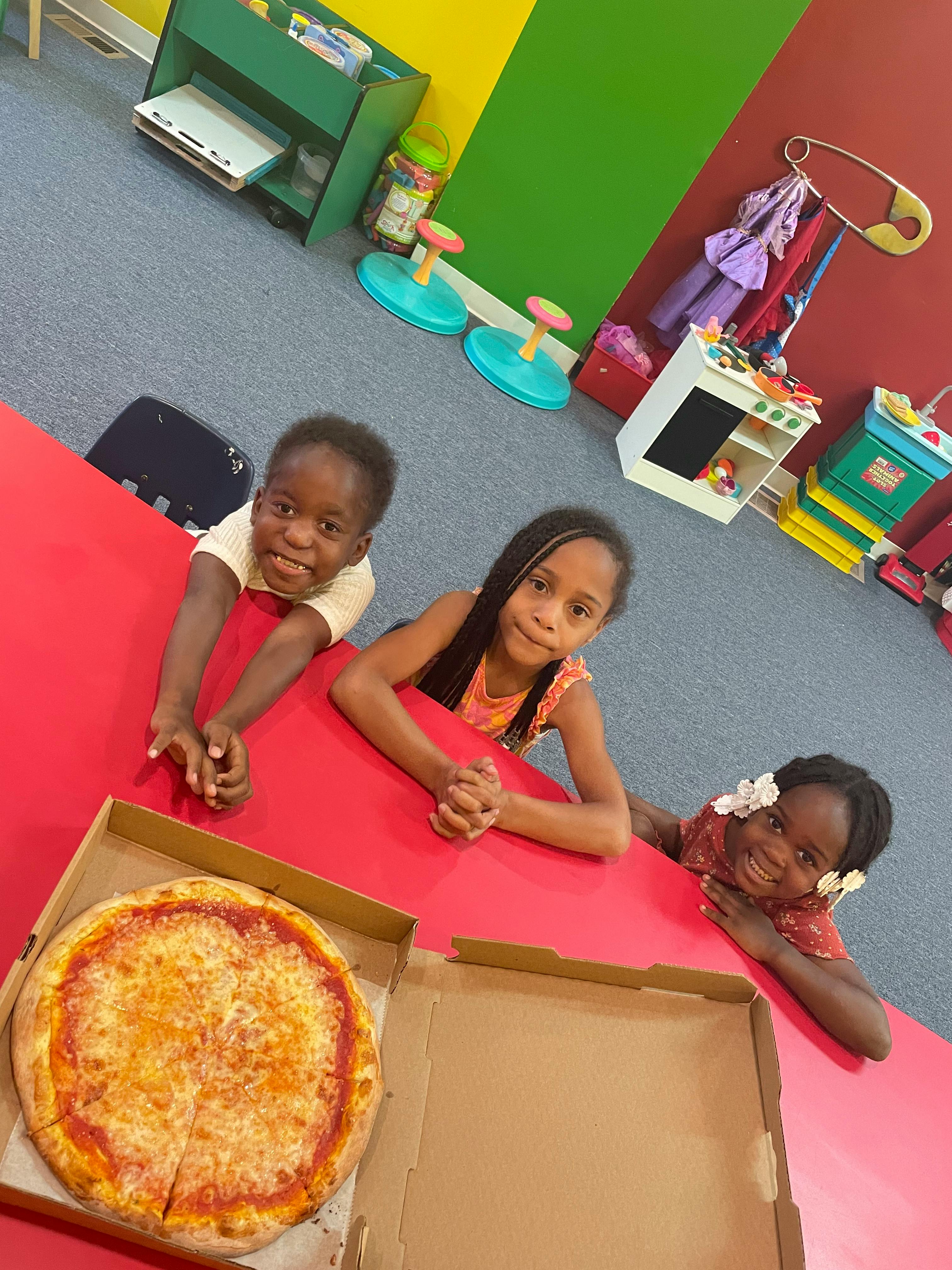 Three children looking at a pizza on a red table