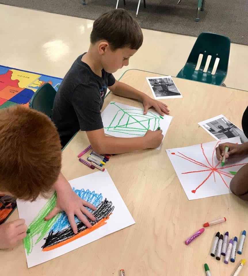 Children drawing with crayons at a table in a classroom