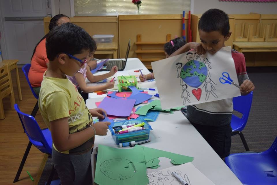 Child holding up a drawing of the Earth, people, and a heart