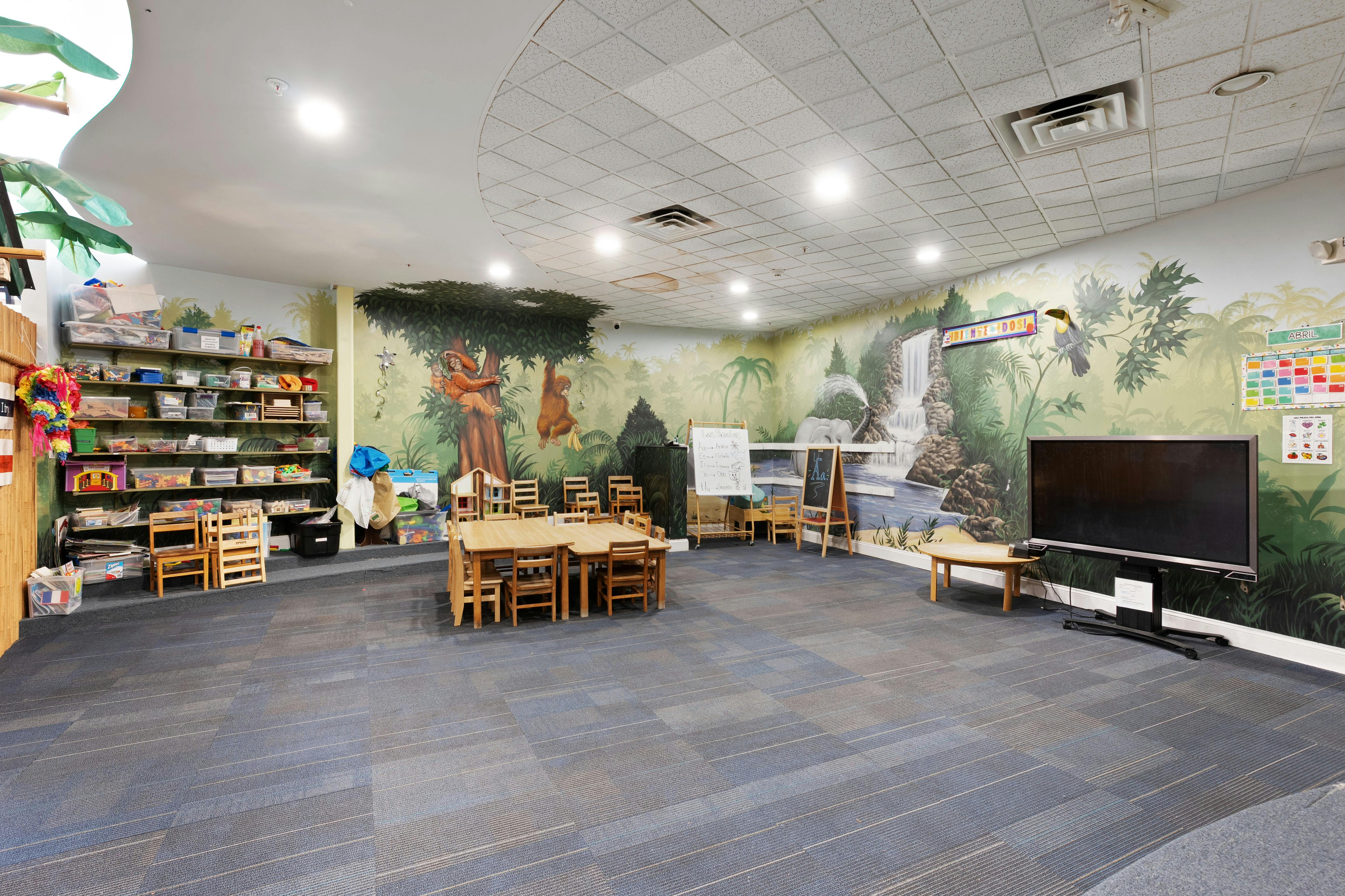 Classroom with jungle-themed wall mural, small wooden tables and chairs