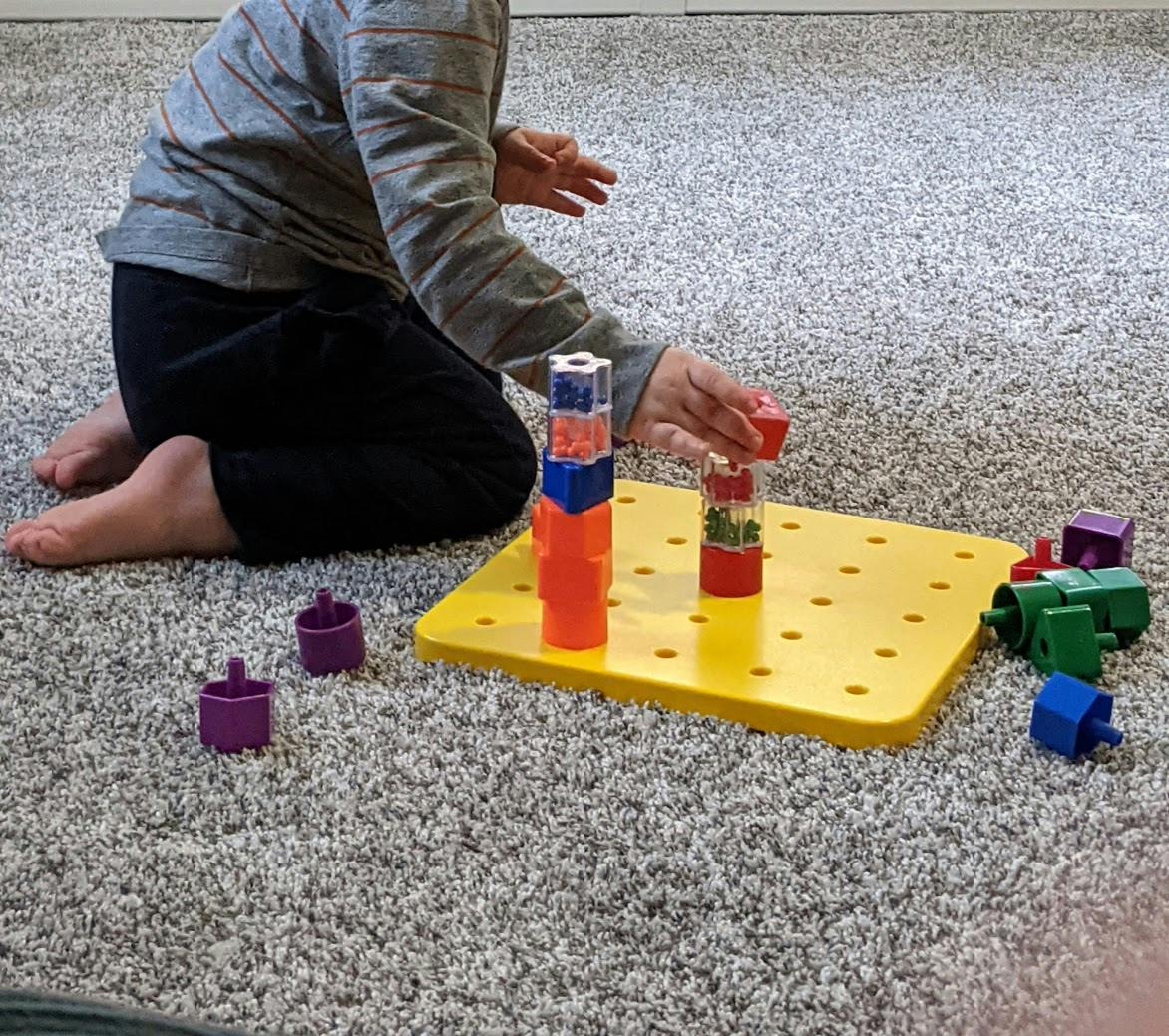 Child kneeling on carpet playing with colorful stacking toys