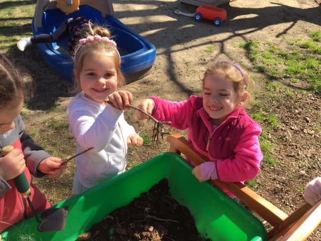 Two children playing with sticks and dirt in a green planter
