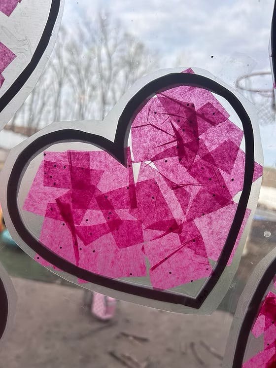 Heart-shaped cutout with pink tissue paper pieces on a window