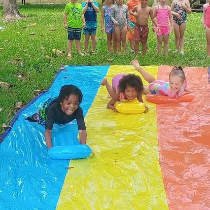 Children playing on a multi-colored water slide on grass
