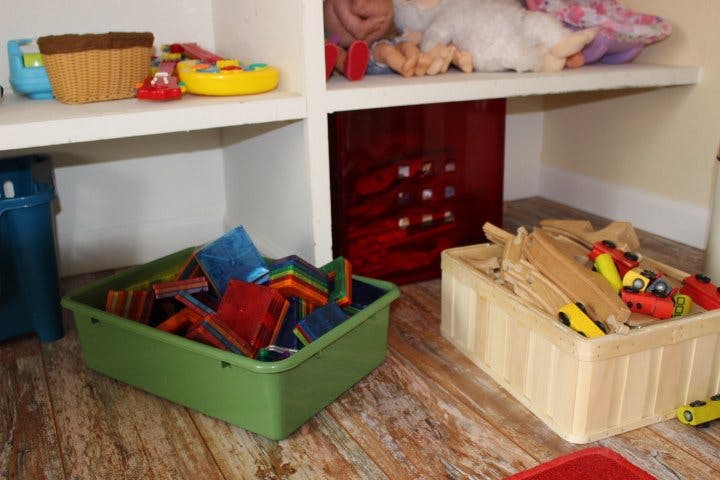 Shelves with toys, including a green bin of blocks and a wooden box of train tracks
