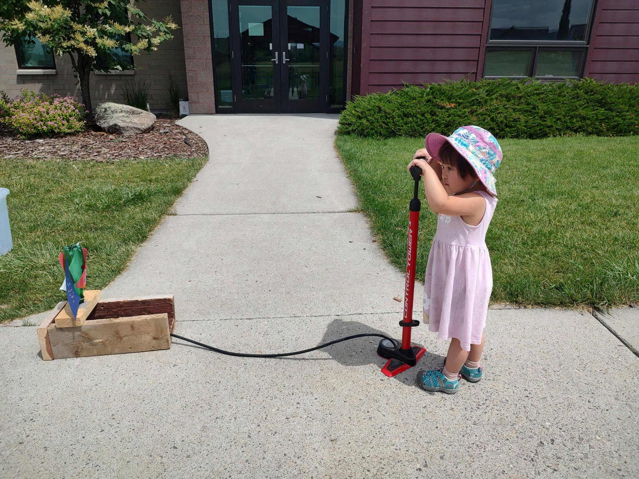 Child operating an air pump connected to a wooden structure with a bottle