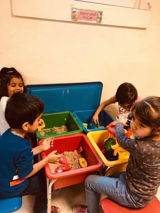 Four children playing with sand and toys in colorful bins