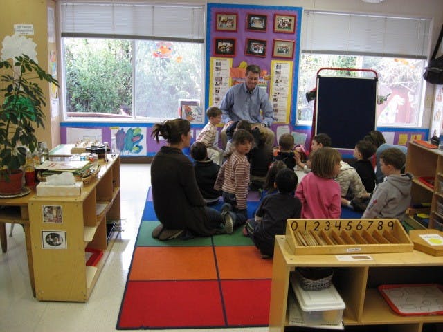 Adults and children sitting on a colorful rug in a classroom