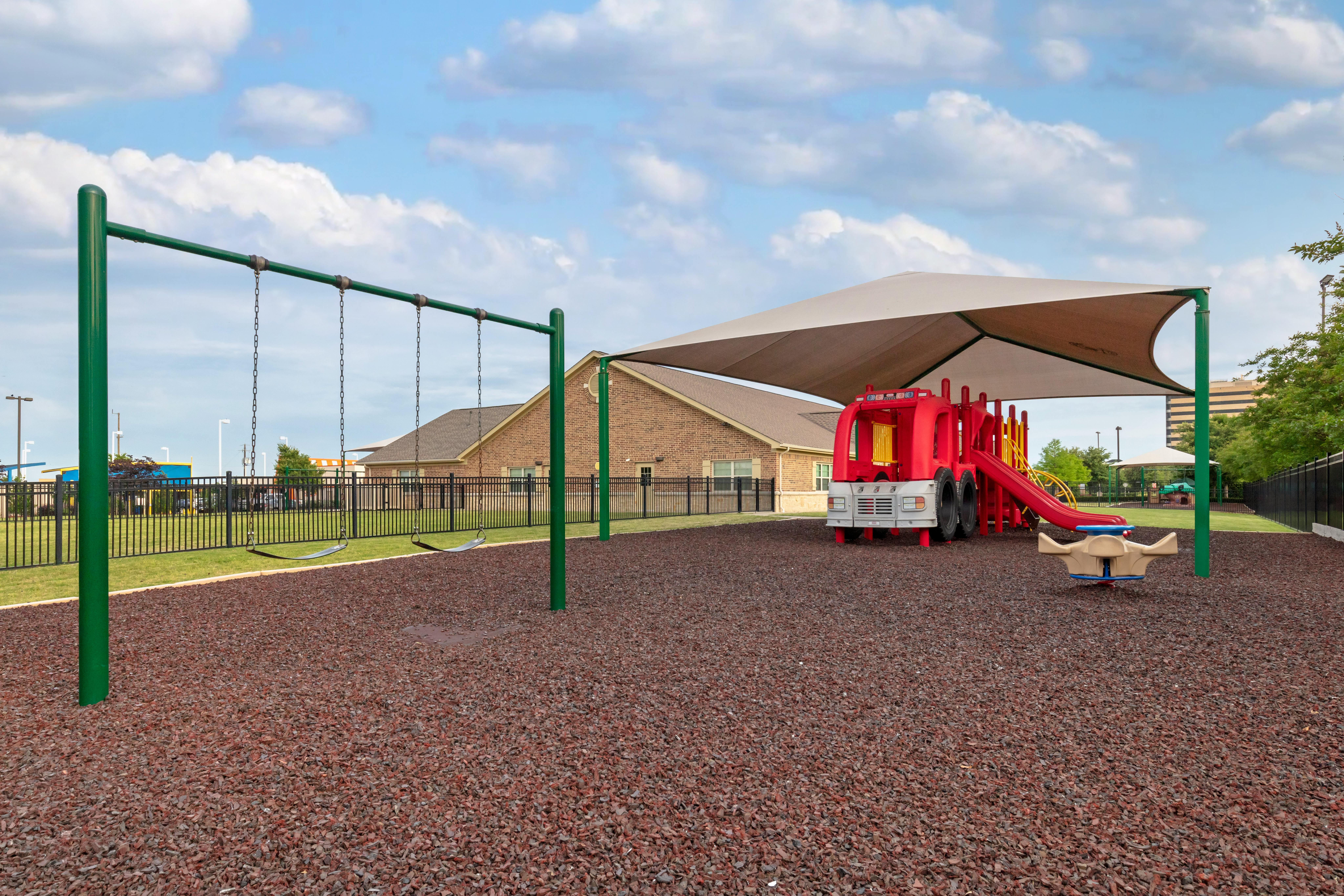 Playground with swings, a red fire truck playset, and a shaded area