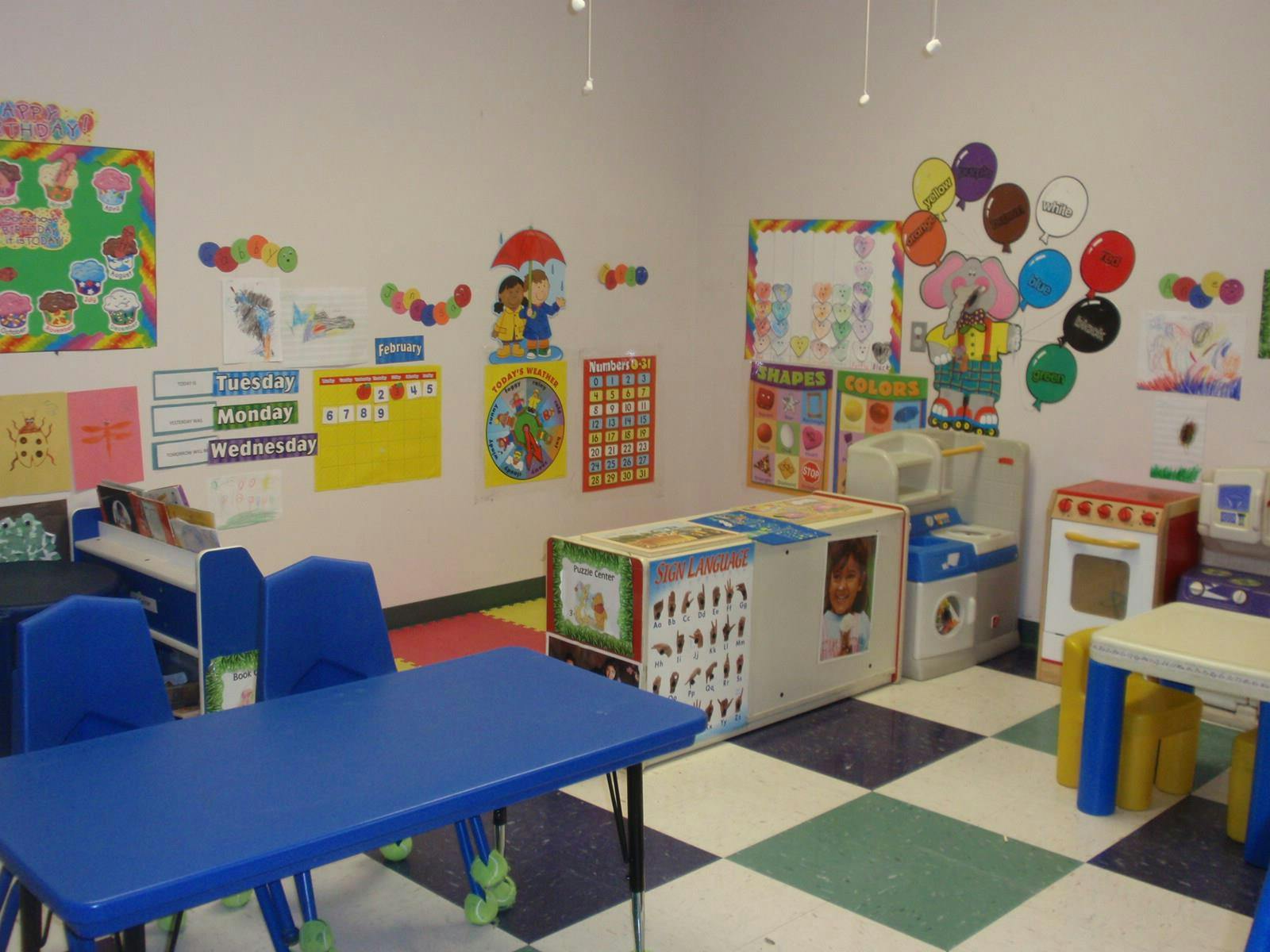Classroom with blue tables and chairs, play kitchen, and wall decorations