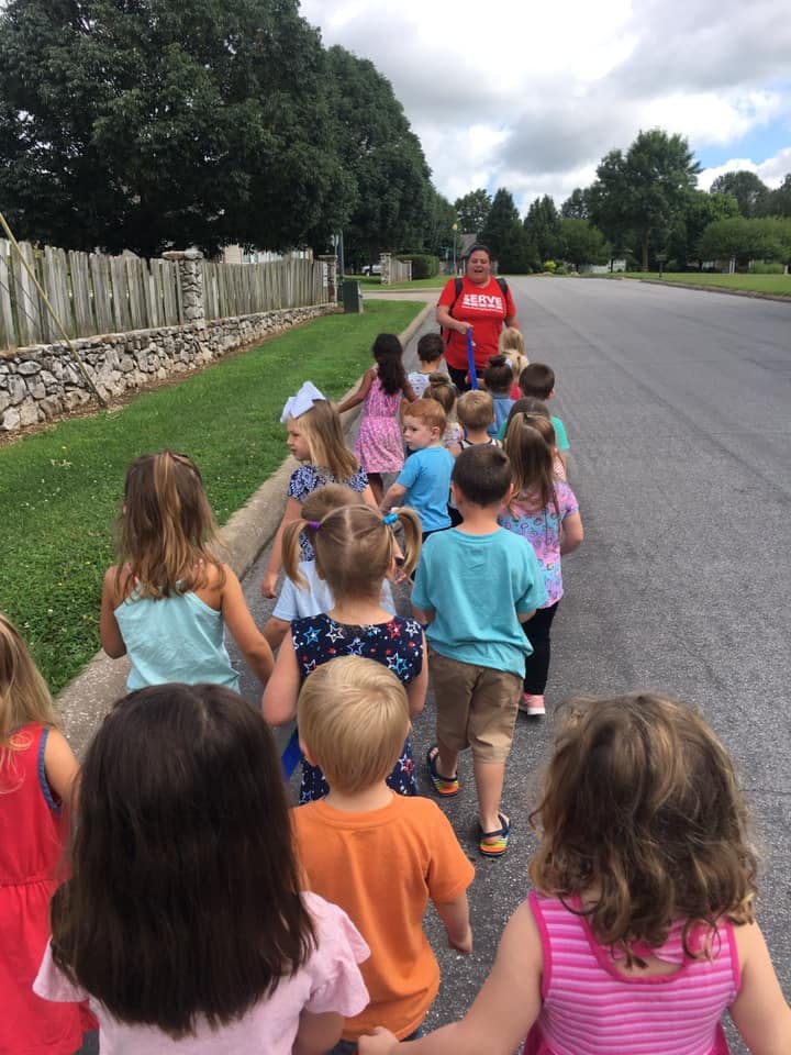 Adult leading a line of children on a sidewalk