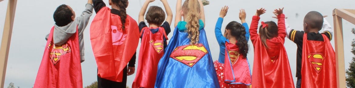 Children in superhero capes with arms raised