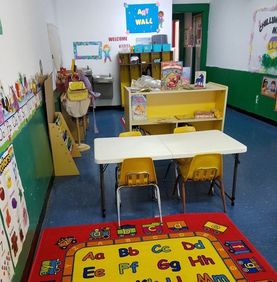 Classroom with small table and chairs, shelves, and an alphabet rug