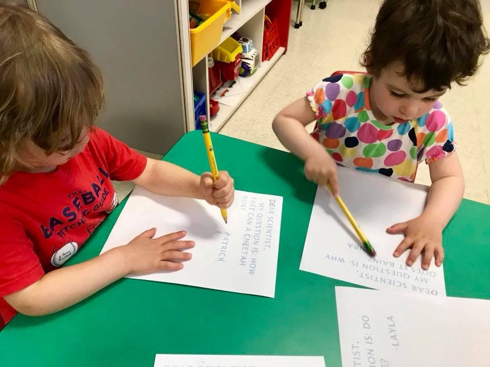 Two children writing on paper with pencils at a table