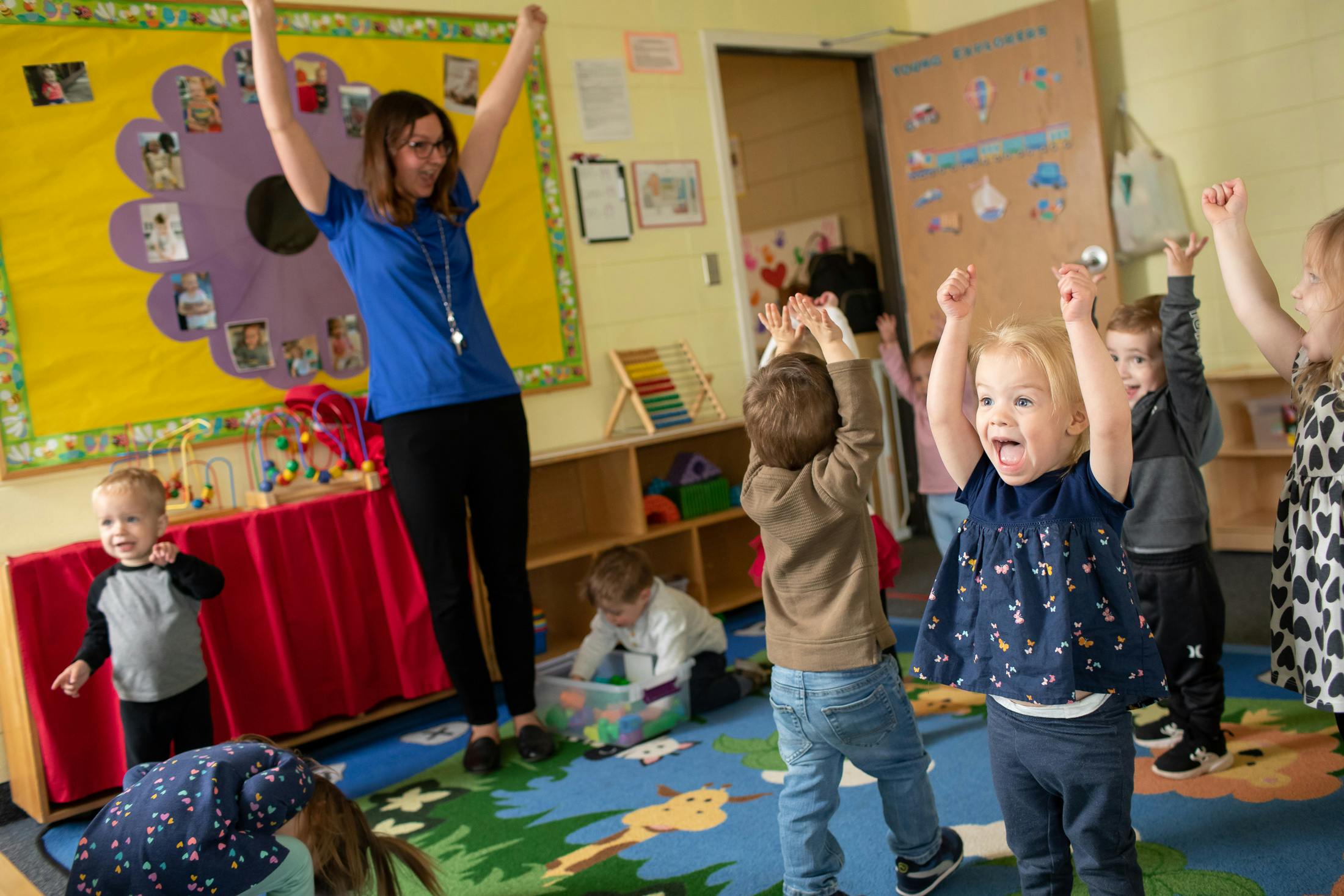 Adult and children with arms raised in a classroom