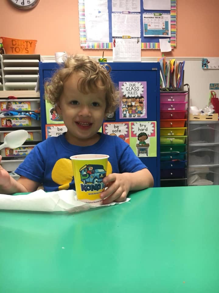 Child sitting at a table holding a cup and spoon