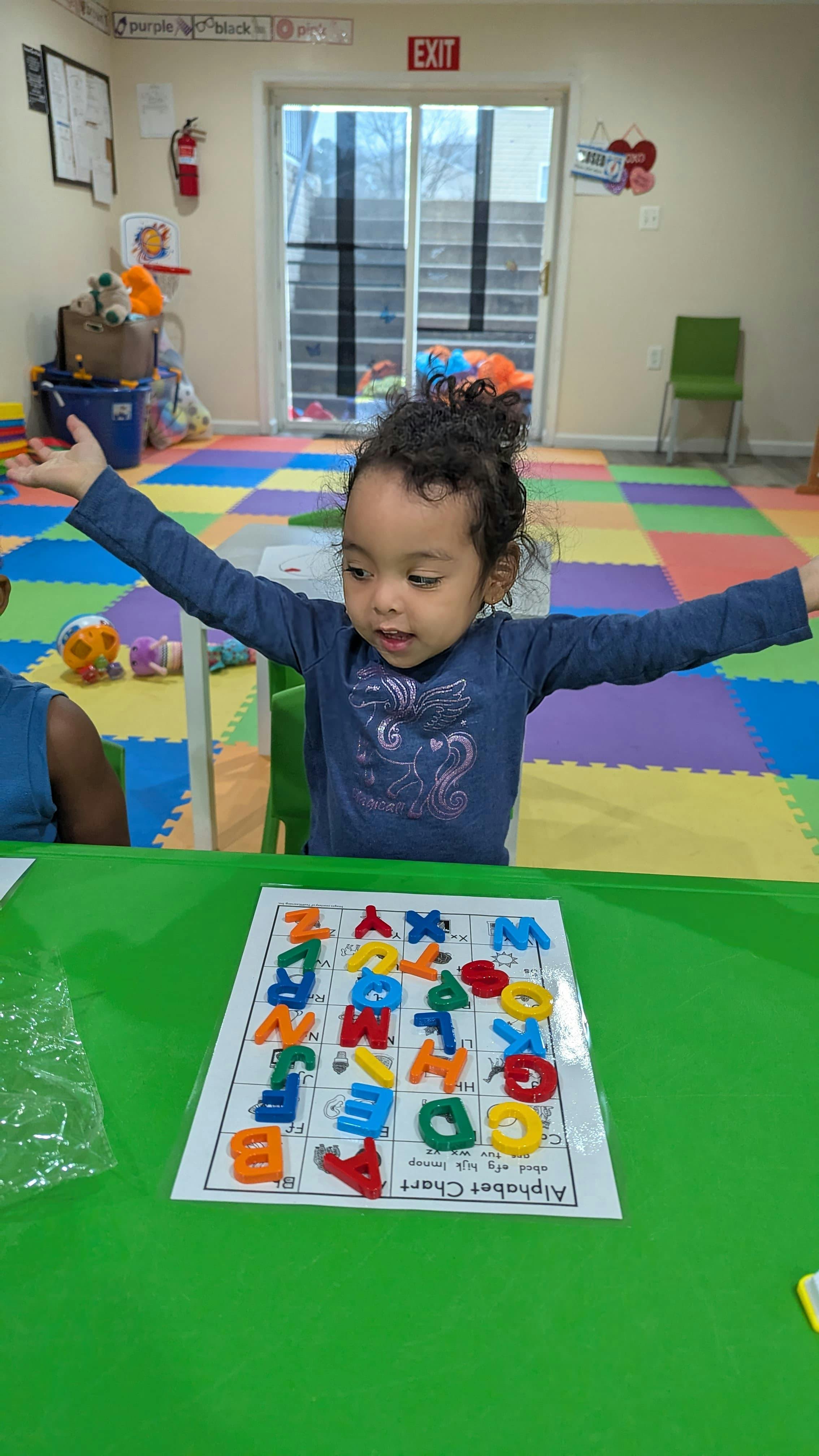Child sitting at a table with a plastic alphabet chart in a playroom
