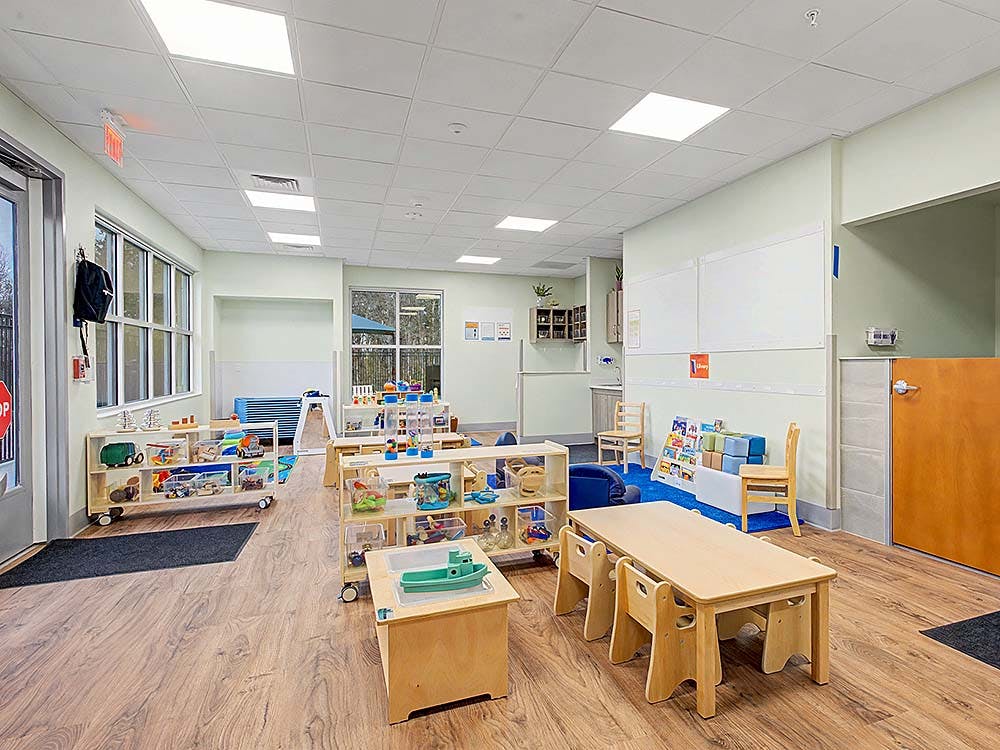 Classroom with small tables, chairs, and shelves of toys