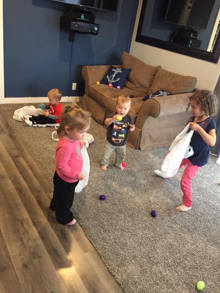 Three children playing with balls and bags on a carpeted floor