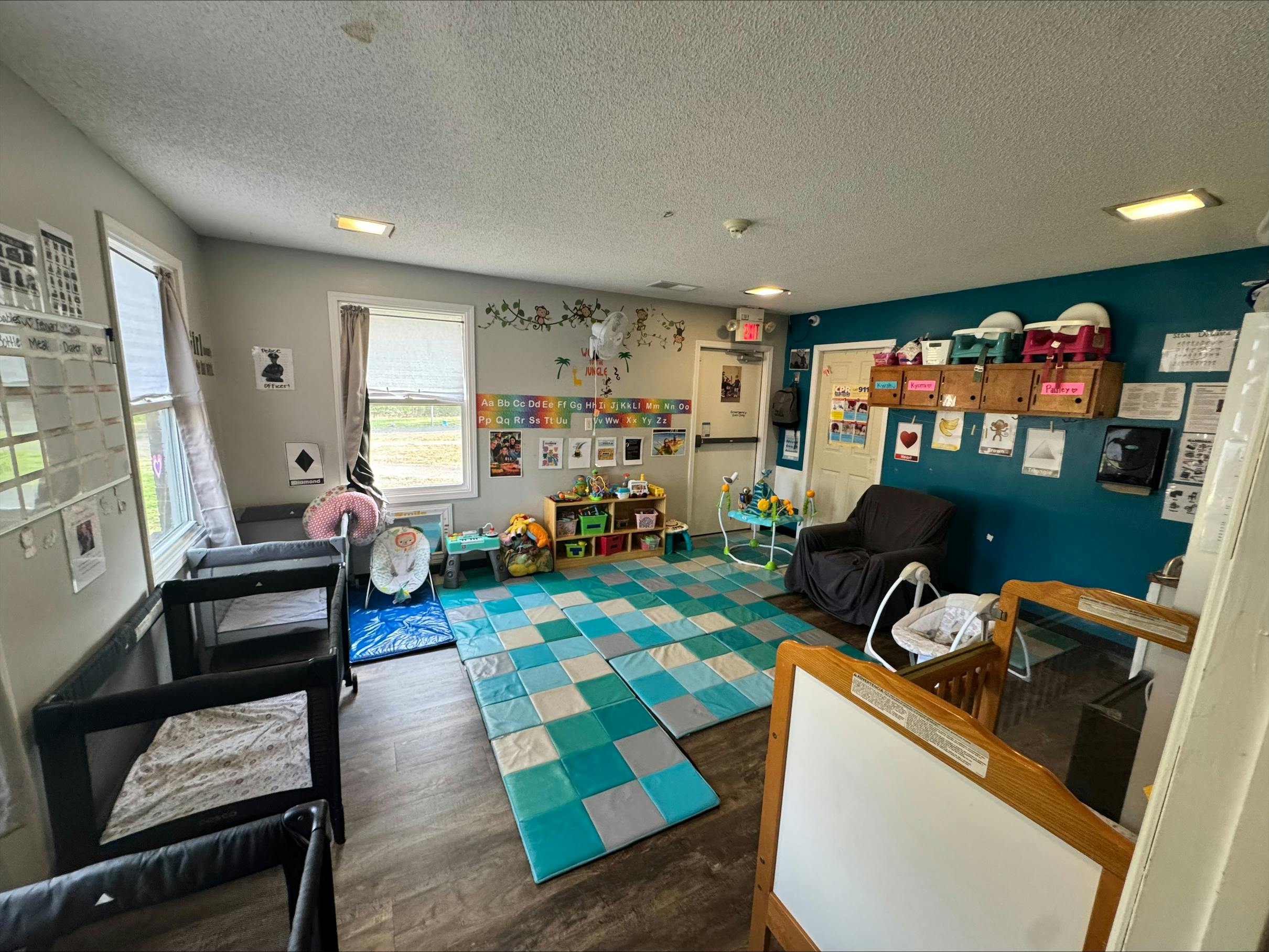Classroom with playmats, two cribs, child seats, and alphabet decorations
