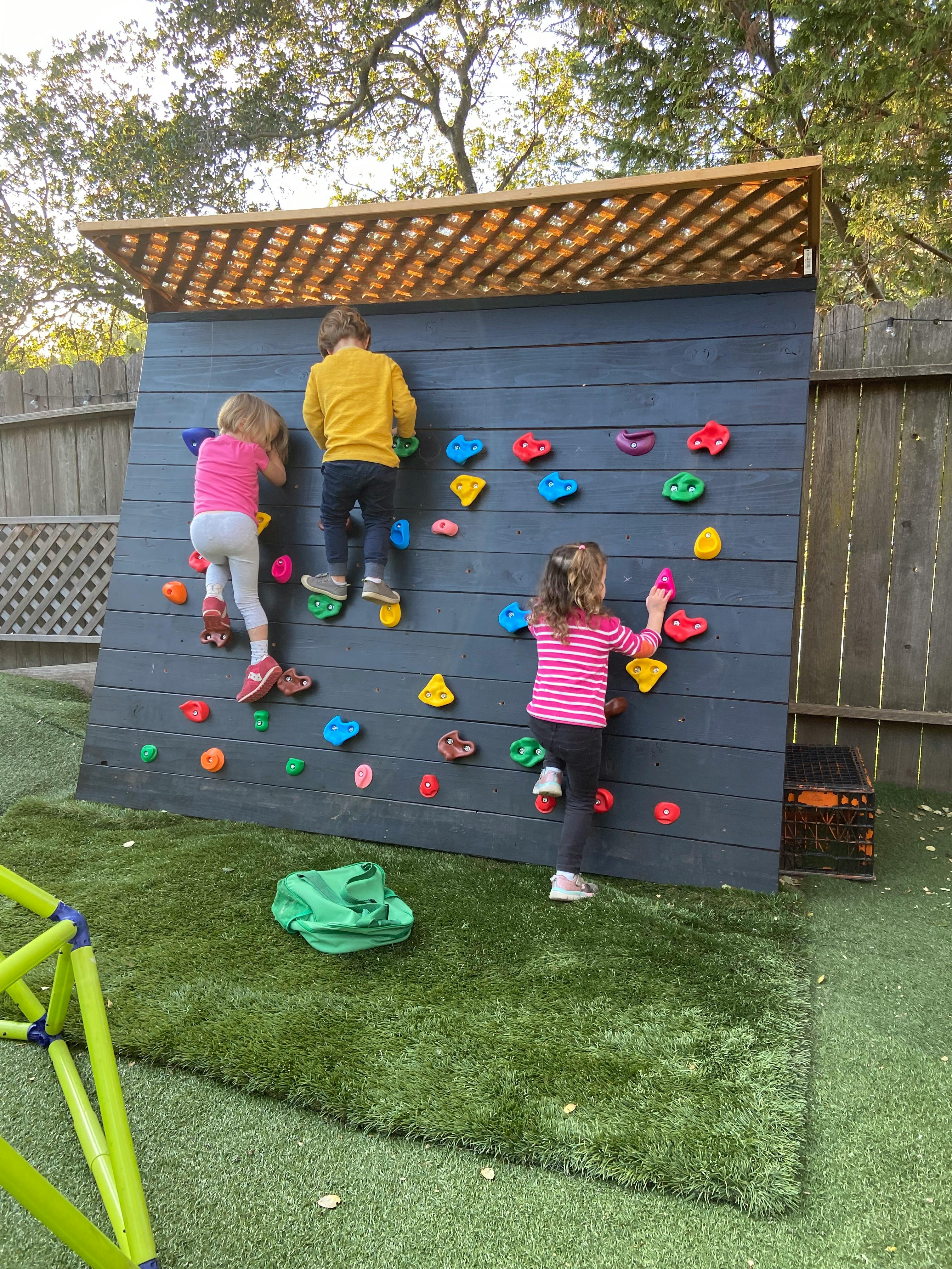 Three children climbing on an outdoor rock wall